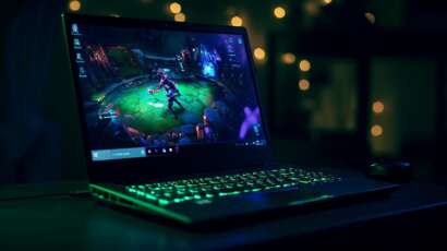 Laptop showing live League of Legends esports match with neon green keyboard lighting in a dark room