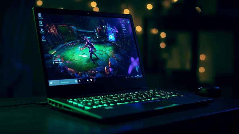 Laptop showing live League of Legends esports match with neon green keyboard lighting in a dark room